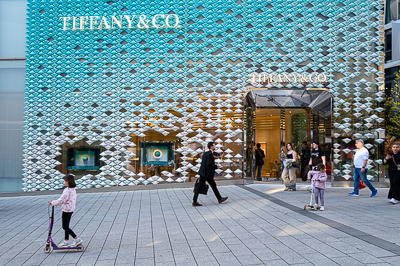 Devant Tiffany&Co, Stuttgart.
Écrin turquoise et brillant d’un joaillier de luxe. À ses pieds, la vie ordinaire file : enfants en trottinette, passants pressés ou curieux. Le contraste dit tout.